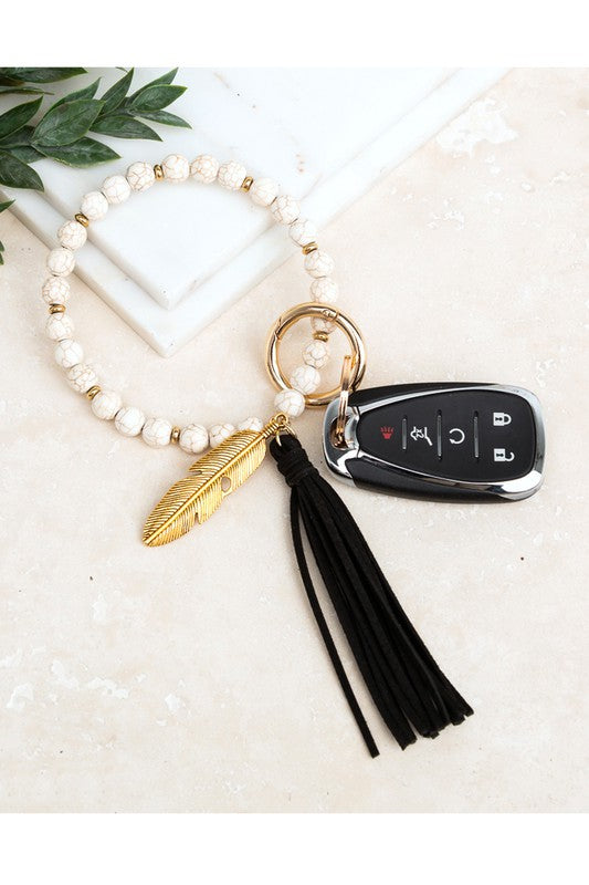 Boho Stone Key Ring Bracelet Earthy, boho vibe featuring genuine stone beads, suede tassel, and feather charm. Key Ring Bracelet Genuine Stone Antique gold feather charm Removable Gold Clasp Removable Gold Key Ring Reinforced Wire design Dimensions: 4" Suede Tassel Gold Accent Beads